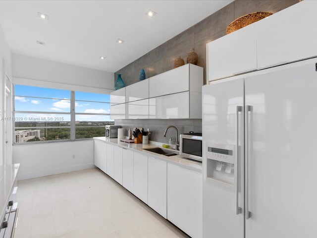 kitchen with high end white fridge, white cabinetry, tasteful backsplash, and sink