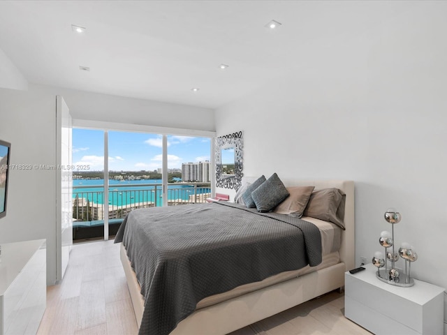 bedroom featuring light hardwood / wood-style flooring, a water view, and access to exterior