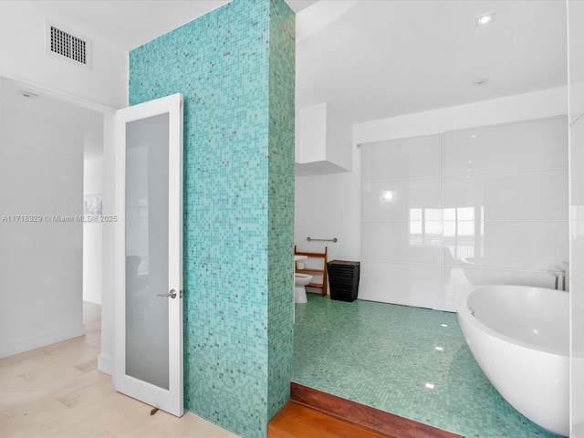 bathroom with a bidet, tile patterned flooring, tile walls, toilet, and a tub to relax in