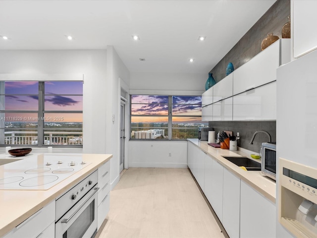 kitchen with sink, white appliances, tasteful backsplash, and white cabinets