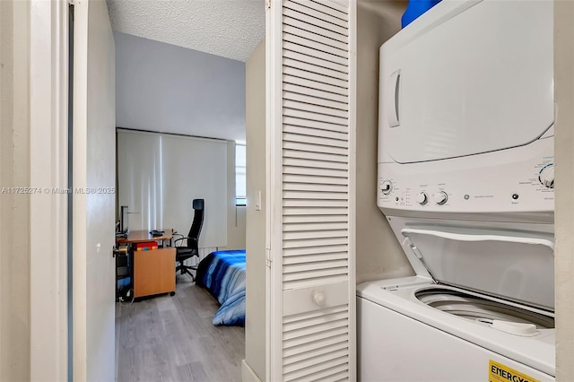 laundry area with stacked washing maching and dryer, light hardwood / wood-style floors, and a textured ceiling