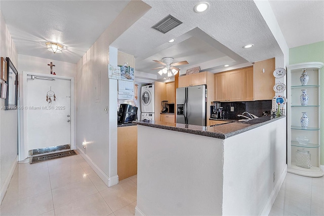 kitchen with kitchen peninsula, stainless steel fridge, light tile patterned floors, decorative backsplash, and stacked washer / drying machine