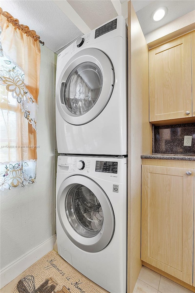 washroom with stacked washer and dryer, a textured ceiling, and light tile patterned flooring