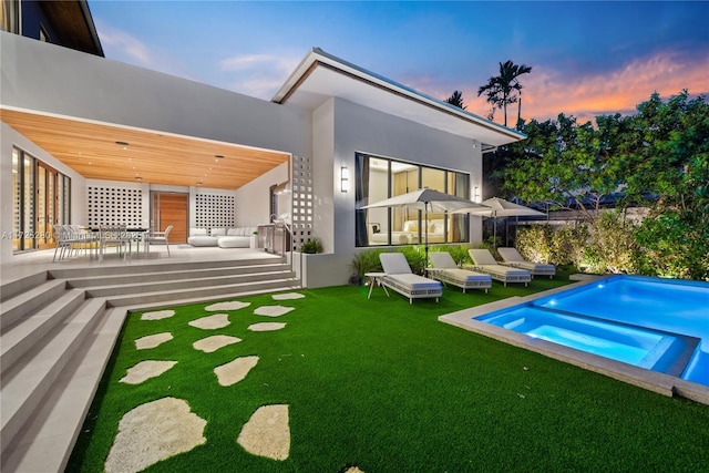 back house at dusk featuring a patio and a lawn