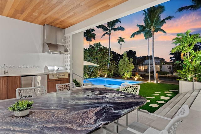 pool at dusk featuring an outdoor kitchen, a grill, and sink