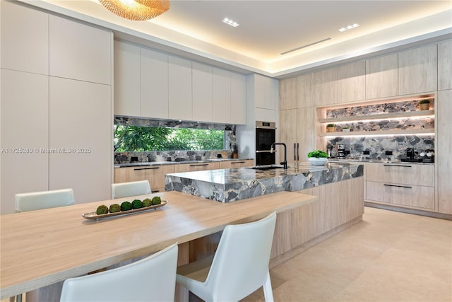 kitchen with sink, light stone counters, a kitchen bar, stainless steel double oven, and a center island with sink