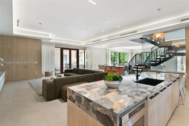 kitchen with an island with sink, light stone countertops, pendant lighting, stainless steel microwave, and sink