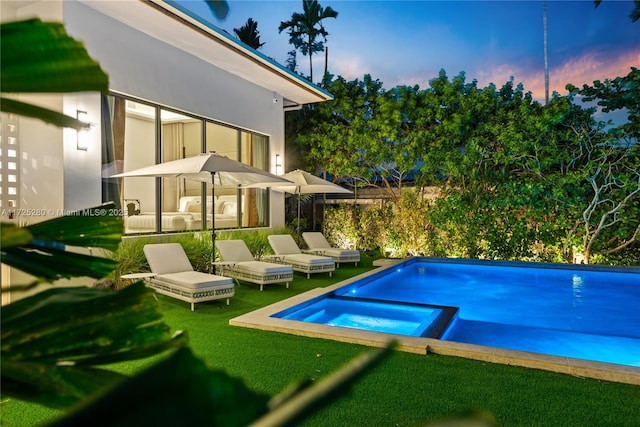 pool at dusk featuring a lawn