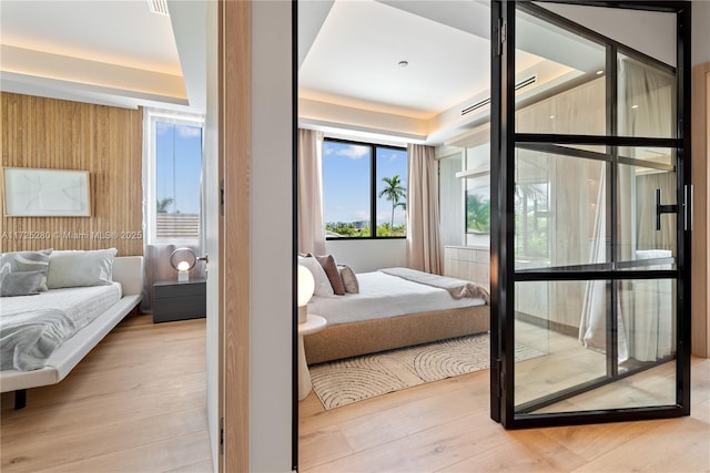 bedroom with light hardwood / wood-style flooring, access to outside, and a raised ceiling