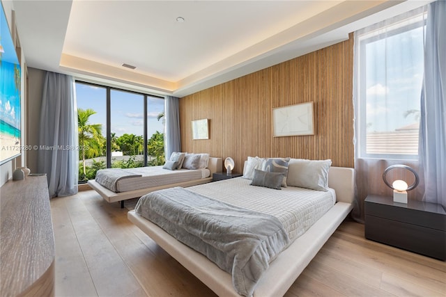 bedroom featuring floor to ceiling windows, light wood-type flooring, wood walls, and access to exterior