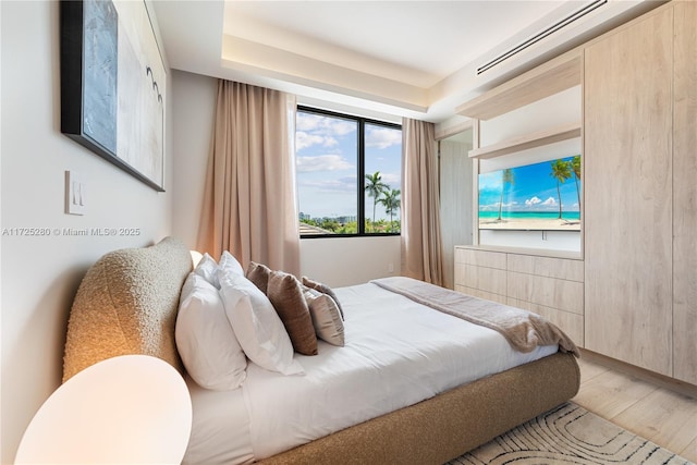 bedroom featuring a raised ceiling and light wood-type flooring