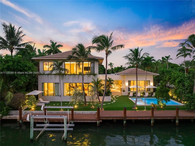 back house at dusk with a balcony, a patio, a yard, and a water view