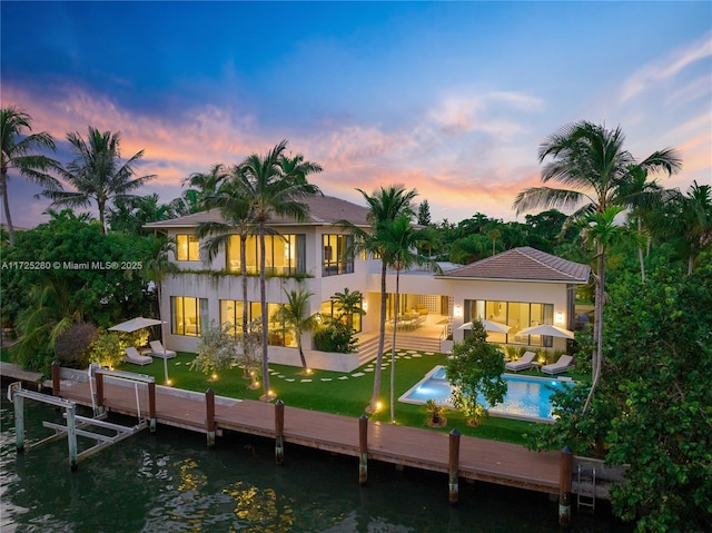 back house at dusk with a patio, a yard, a balcony, and a water view