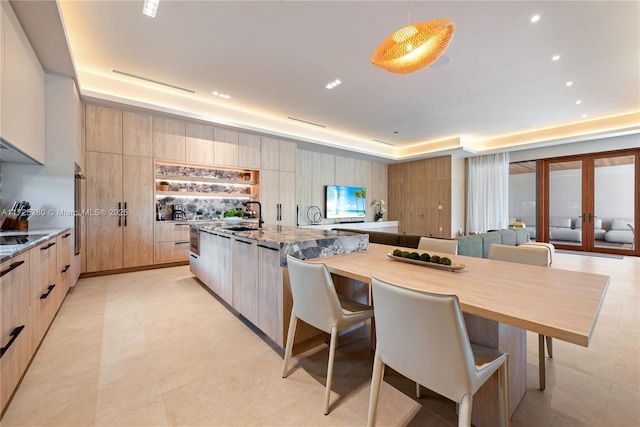 kitchen with sink, a center island, light brown cabinets, a kitchen breakfast bar, and light stone countertops