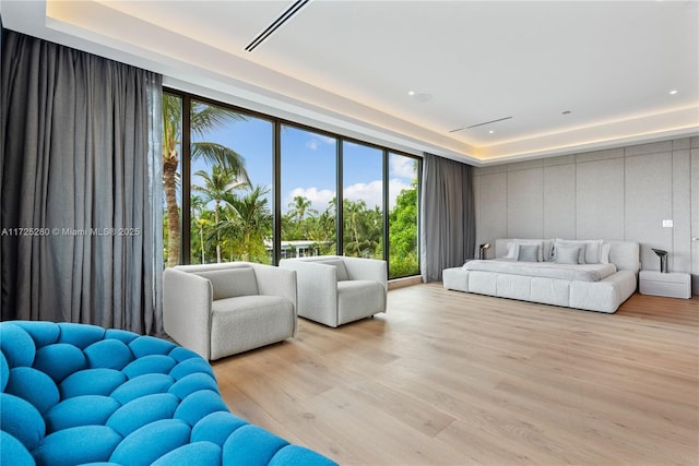 living room with a raised ceiling, light wood-type flooring, and floor to ceiling windows