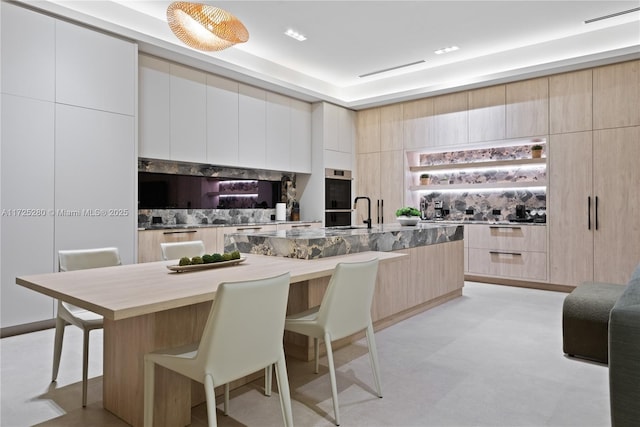 kitchen featuring a center island with sink, double oven, a kitchen breakfast bar, and light brown cabinetry