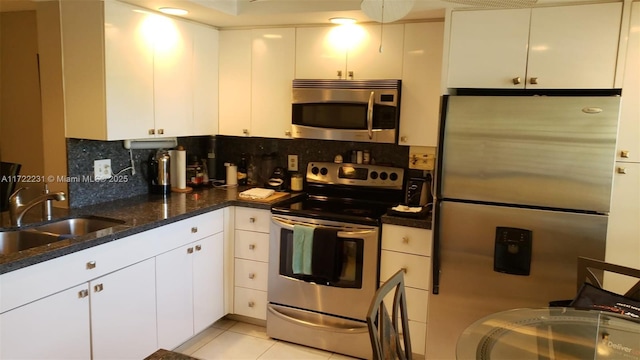 kitchen with sink, white cabinets, light tile patterned floors, dark stone counters, and appliances with stainless steel finishes