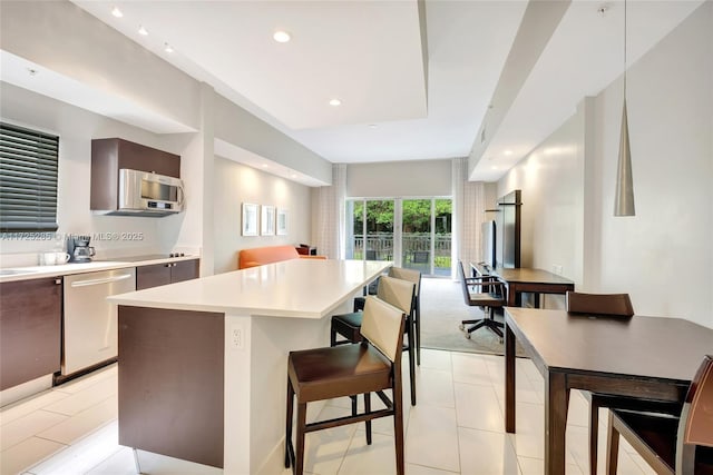 kitchen featuring a kitchen island, stainless steel dishwasher, light tile patterned floors, and a kitchen breakfast bar