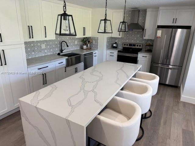 kitchen with wall chimney exhaust hood, pendant lighting, stainless steel appliances, a breakfast bar, and a kitchen island