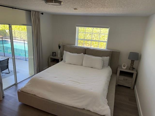 bedroom with access to exterior, a textured ceiling, and dark wood-type flooring