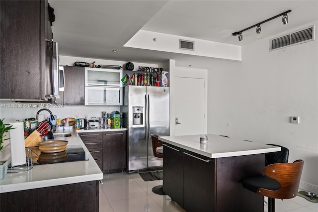 kitchen with stainless steel fridge, light tile patterned floors, a kitchen bar, dark brown cabinets, and sink