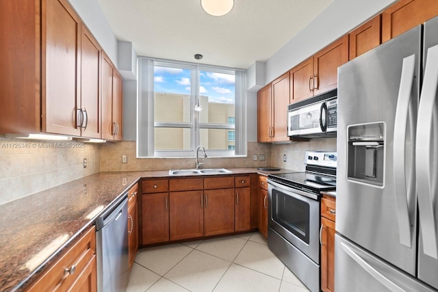 kitchen with stainless steel appliances, sink, dark stone countertops, light tile patterned floors, and backsplash