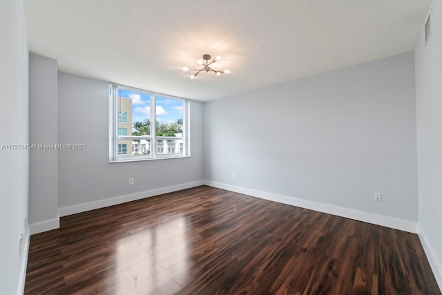 unfurnished room with dark wood-type flooring, a textured ceiling, and a chandelier