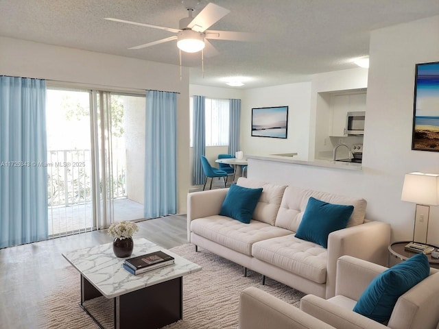 living room featuring ceiling fan, a textured ceiling, and light wood-type flooring