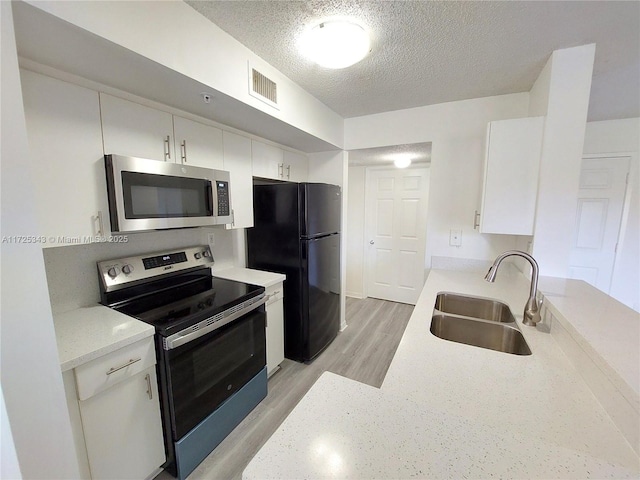 kitchen featuring sink, stainless steel appliances, light hardwood / wood-style floors, a textured ceiling, and white cabinets