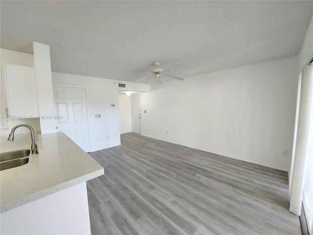 living room with ceiling fan, sink, a textured ceiling, and light wood-type flooring