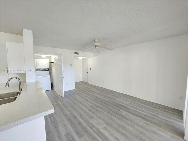 unfurnished living room with sink, ceiling fan, a textured ceiling, washer / clothes dryer, and light wood-type flooring