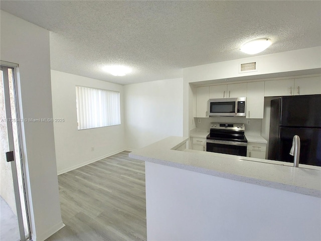 kitchen with appliances with stainless steel finishes, a textured ceiling, light wood-type flooring, and kitchen peninsula