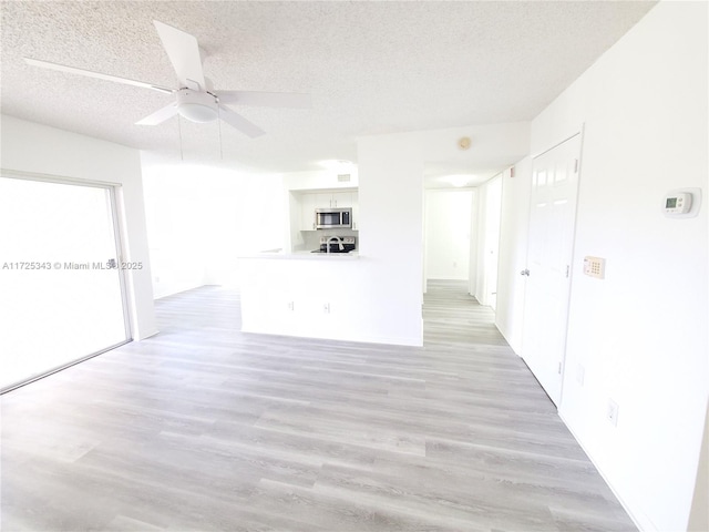 unfurnished living room with ceiling fan, light wood-type flooring, and a textured ceiling