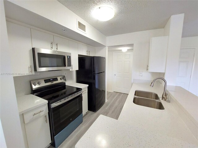 kitchen with sink, white cabinetry, a textured ceiling, light wood-type flooring, and appliances with stainless steel finishes