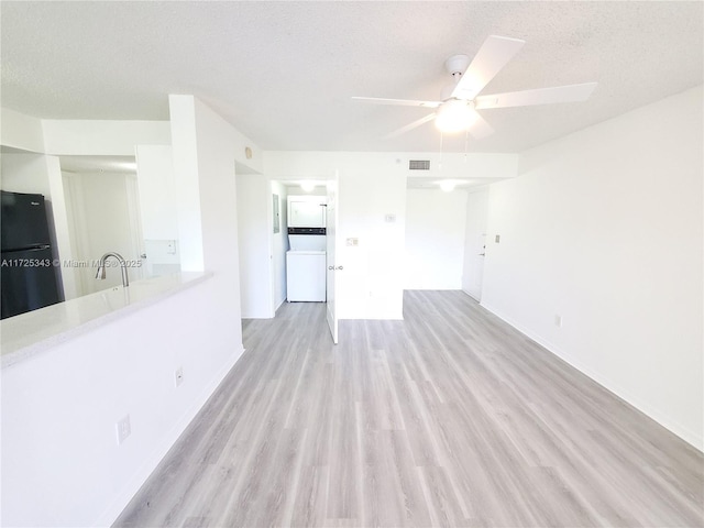 unfurnished living room featuring ceiling fan, light wood-style floors, washer / clothes dryer, baseboards, and visible vents
