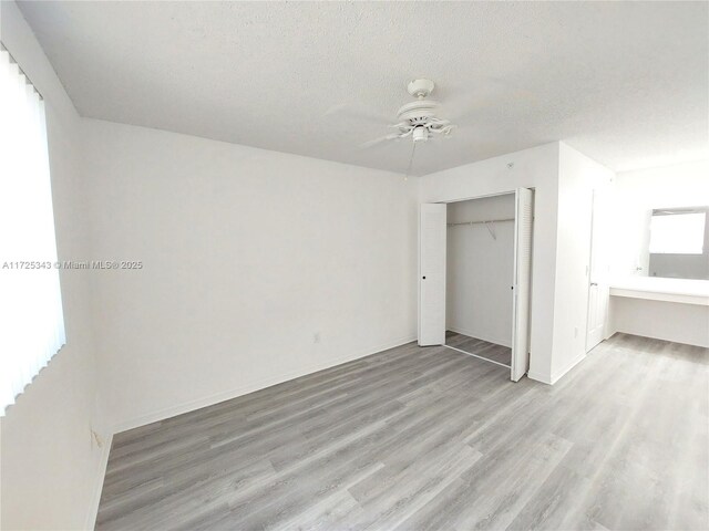 unfurnished bedroom featuring ceiling fan, a textured ceiling, light hardwood / wood-style floors, and a closet