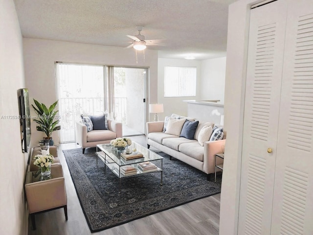 living room with ceiling fan, a textured ceiling, and light wood-type flooring