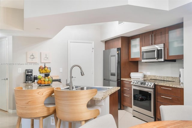 kitchen featuring appliances with stainless steel finishes, light tile patterned floors, a kitchen bar, light stone counters, and sink