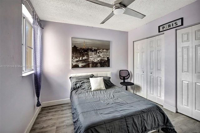 bedroom with wood-type flooring, two closets, ceiling fan, and a textured ceiling