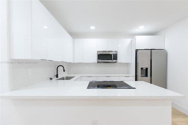 kitchen with sink, stainless steel appliances, white cabinetry, and kitchen peninsula