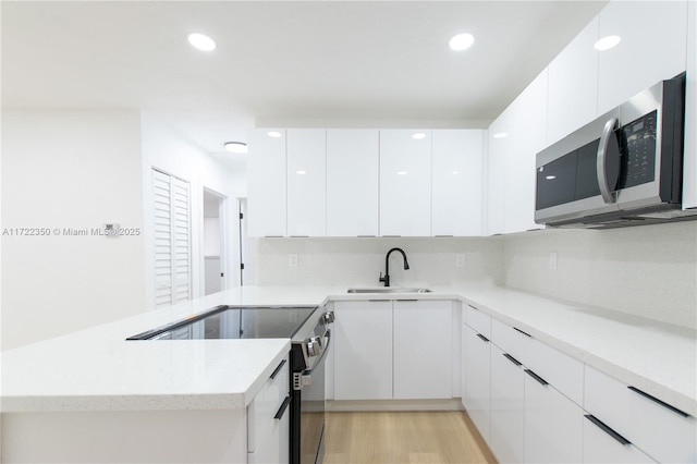 kitchen with kitchen peninsula, electric range, white cabinets, and sink