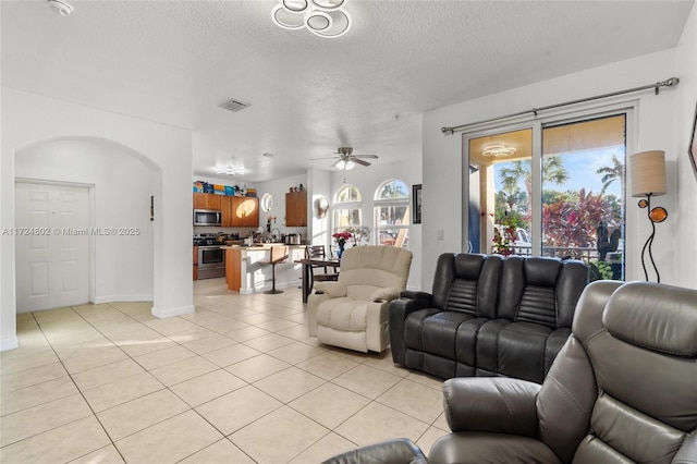 living room with ceiling fan, a textured ceiling, and light tile patterned flooring