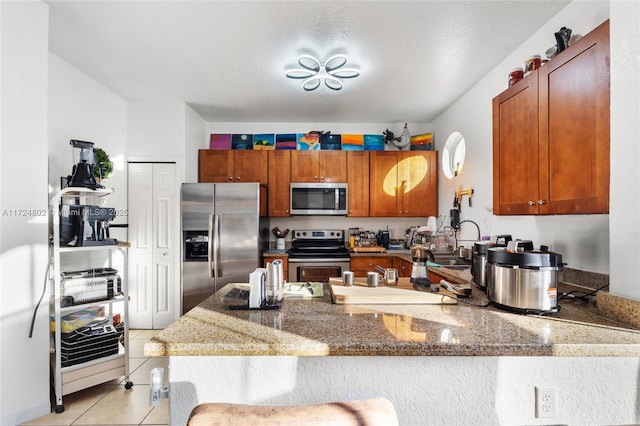 kitchen with light tile patterned floors, sink, appliances with stainless steel finishes, kitchen peninsula, and dark stone counters