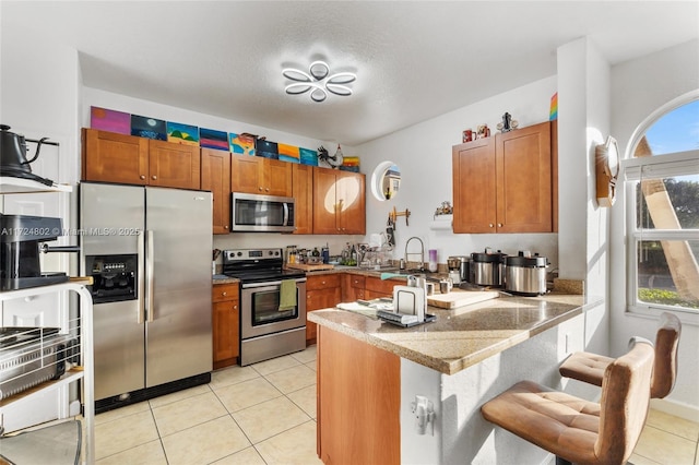 kitchen with appliances with stainless steel finishes, kitchen peninsula, light tile patterned floors, and a wealth of natural light