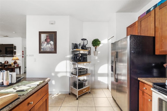 kitchen featuring stainless steel refrigerator with ice dispenser, light tile patterned flooring, and dark stone countertops