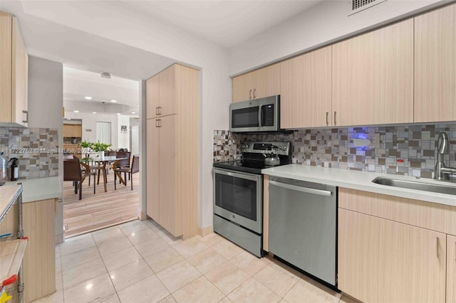 kitchen featuring stainless steel appliances, backsplash, light brown cabinets, and sink