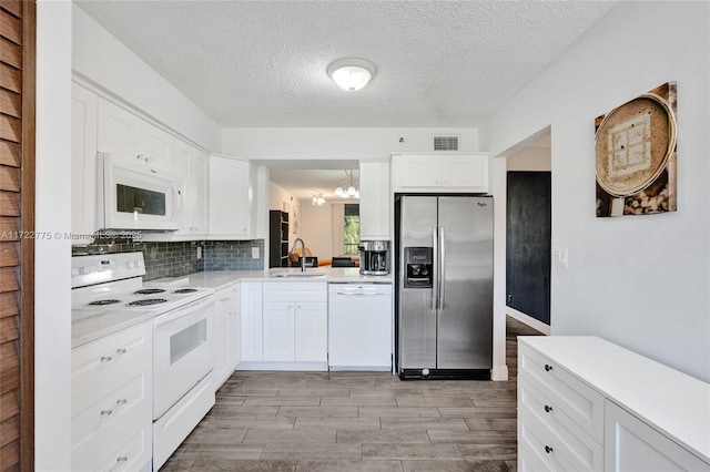 kitchen featuring white appliances, a notable chandelier, a textured ceiling, white cabinets, and sink