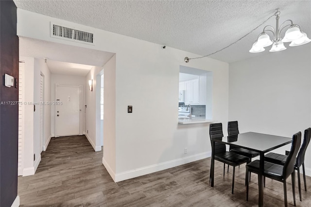 dining space featuring hardwood / wood-style flooring, a textured ceiling, and a notable chandelier