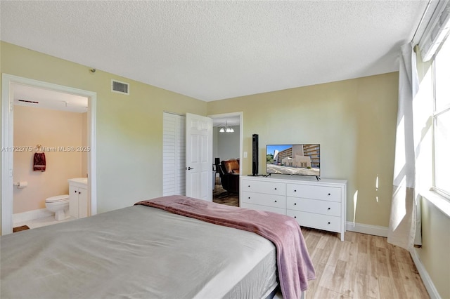 bedroom with a textured ceiling, an inviting chandelier, light hardwood / wood-style floors, a closet, and ensuite bath