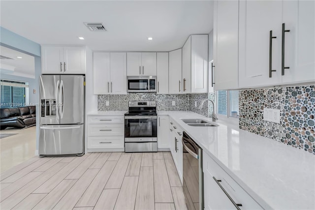 kitchen with light stone countertops, stainless steel appliances, decorative backsplash, white cabinetry, and sink